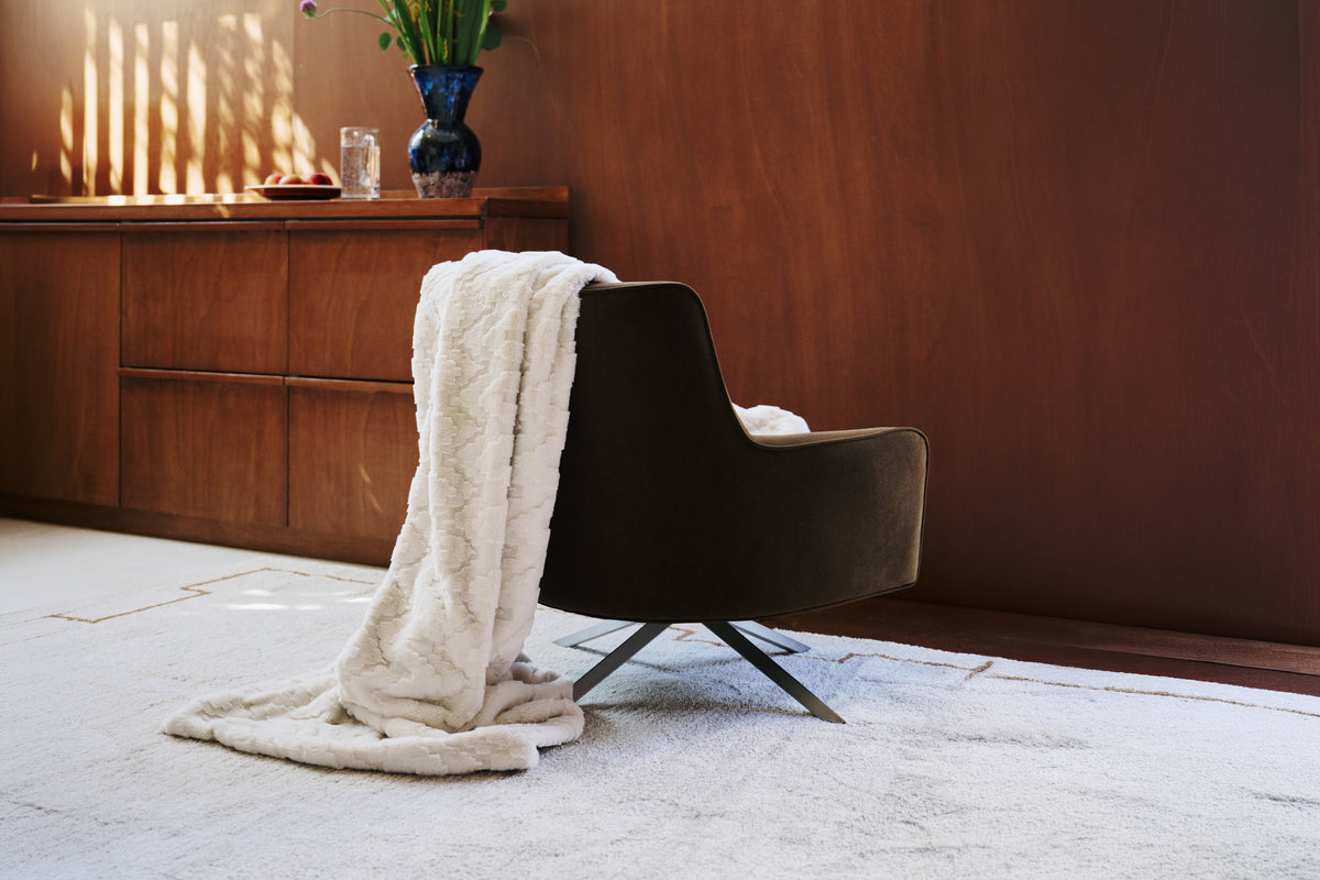 plaid EVEREST en fausse fourrure beige jeté sur un fauteuil pivotant en velours kaki