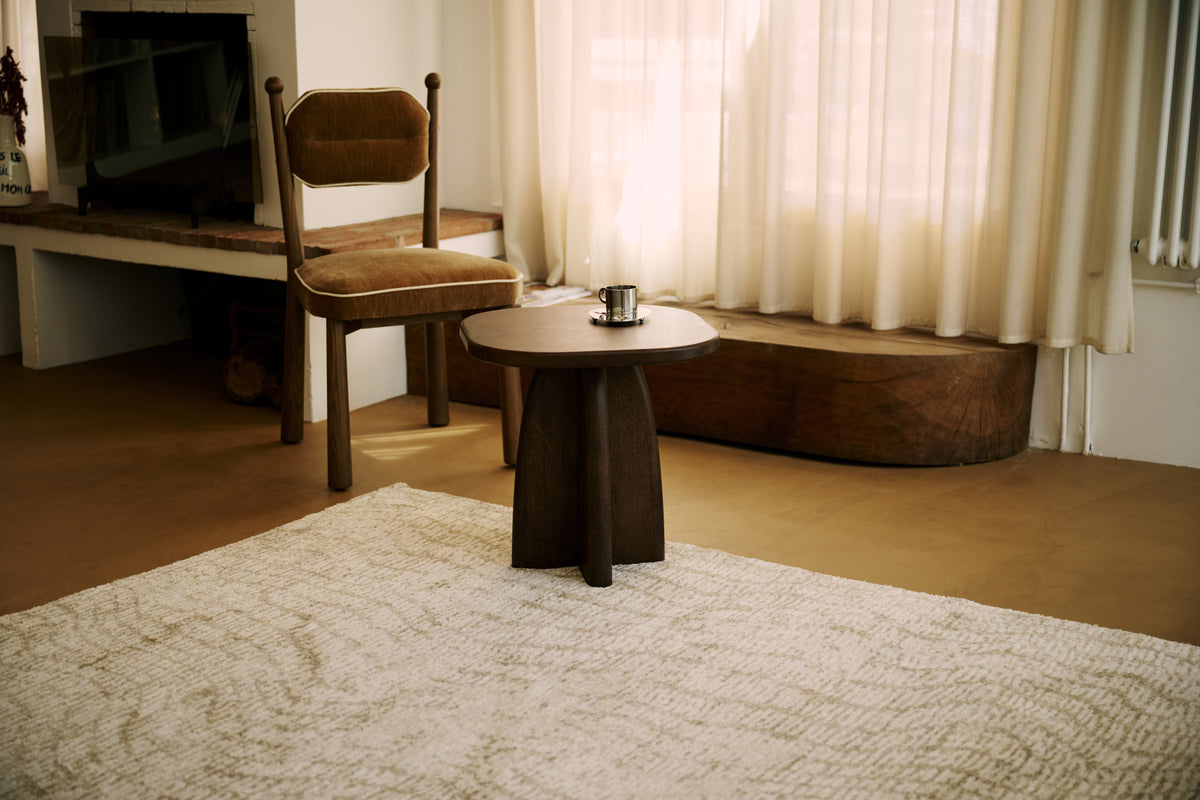 tapis de salon Cortex écru au pied d'une chaise en velours ocre et d'un guéridon en bois
