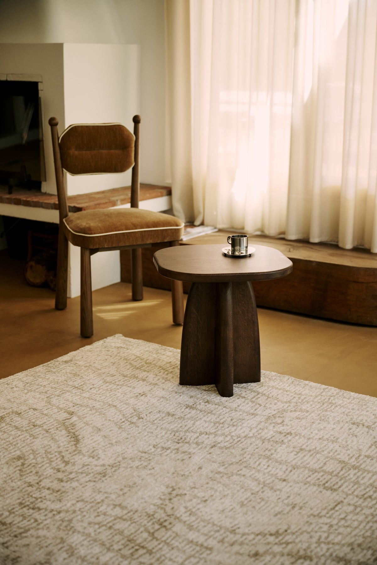 salon à cheminée avec tapis Cortex écru, chaise en velours ocre et guéridon en chêne foncé
