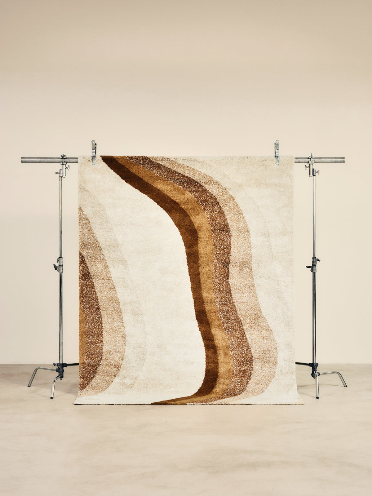 tapis de salon Levante écru à grande vague dégradée caramel suspendu sur un portant