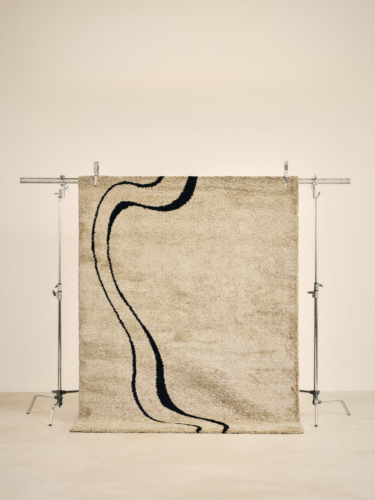 tapis de salon Drift beige sable à double courbe noire suspendu sur un portant de studio