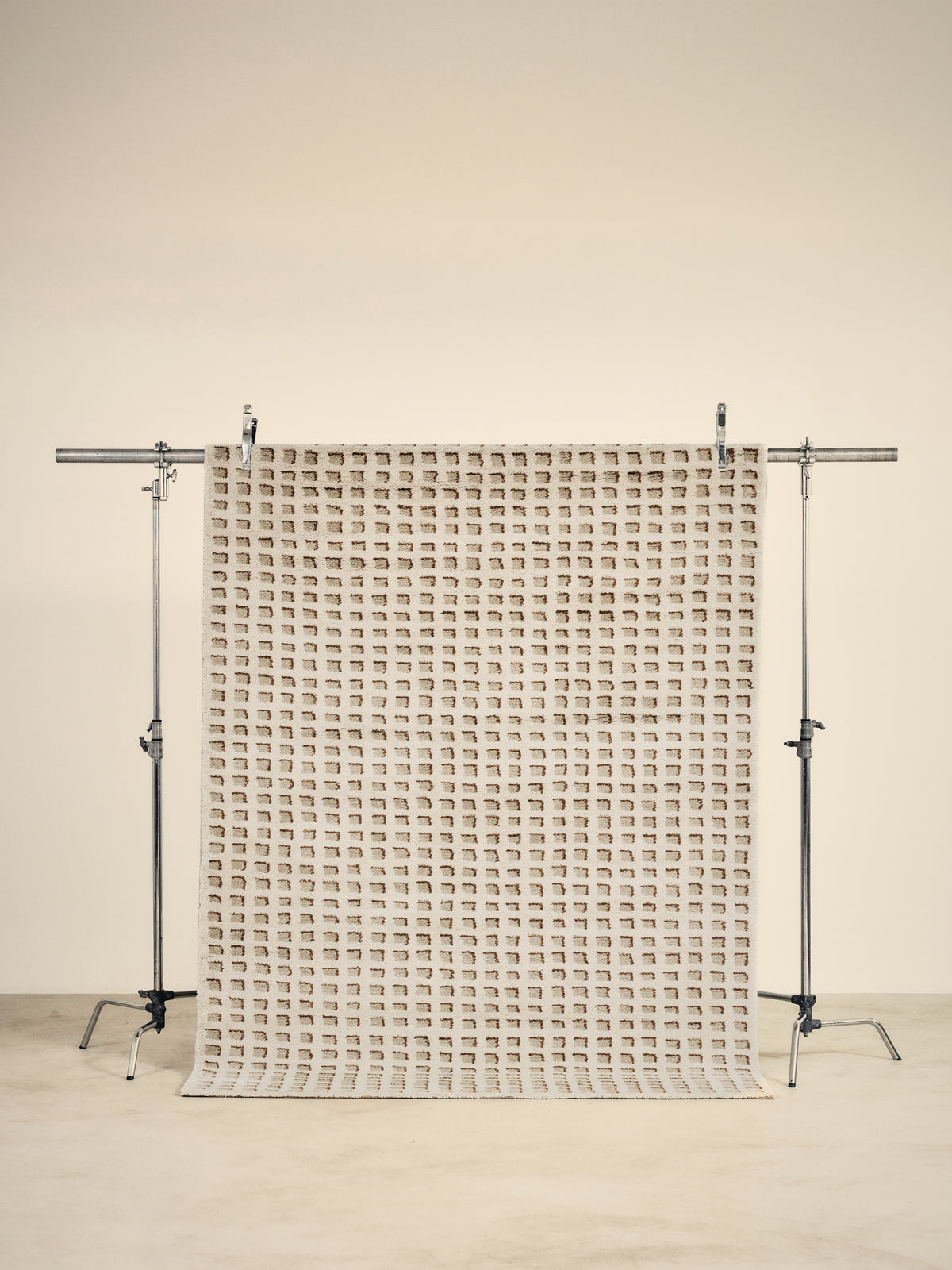 tapis de salon Weave écru à fin damier caramel suspendu sur un portant de studio