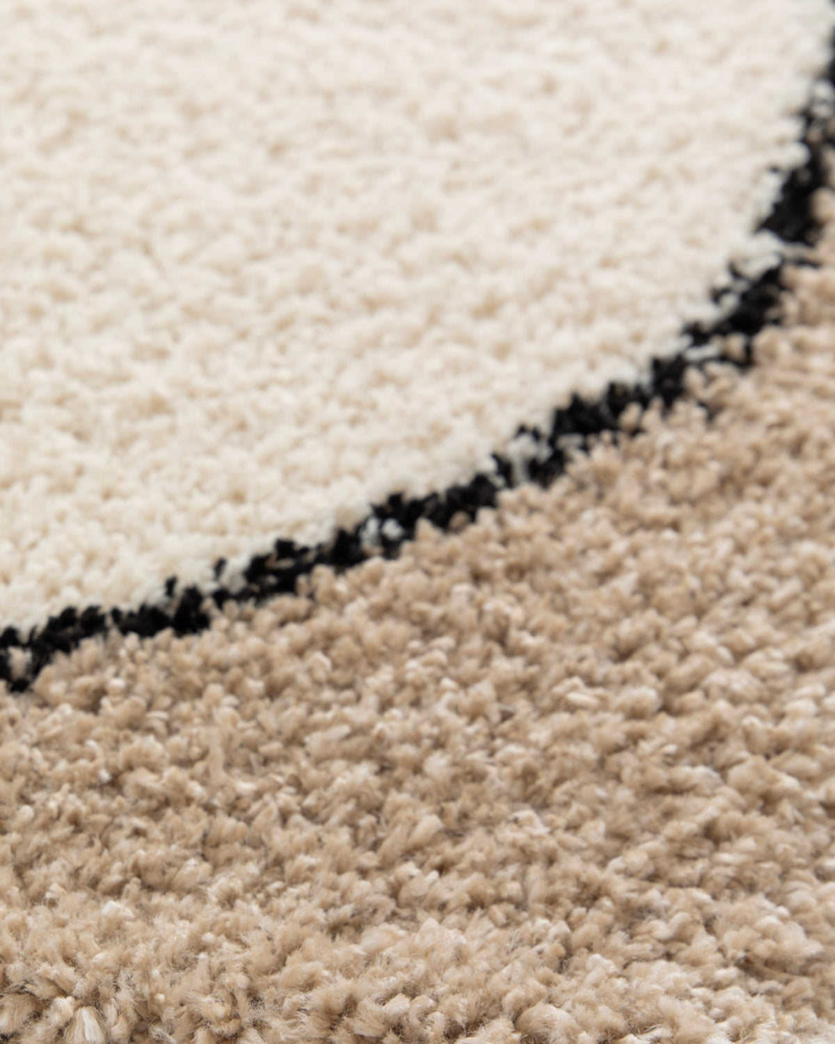 gros plan sur l'angle arrondi du tracé noir sur le velours écru d'un tapis Kento