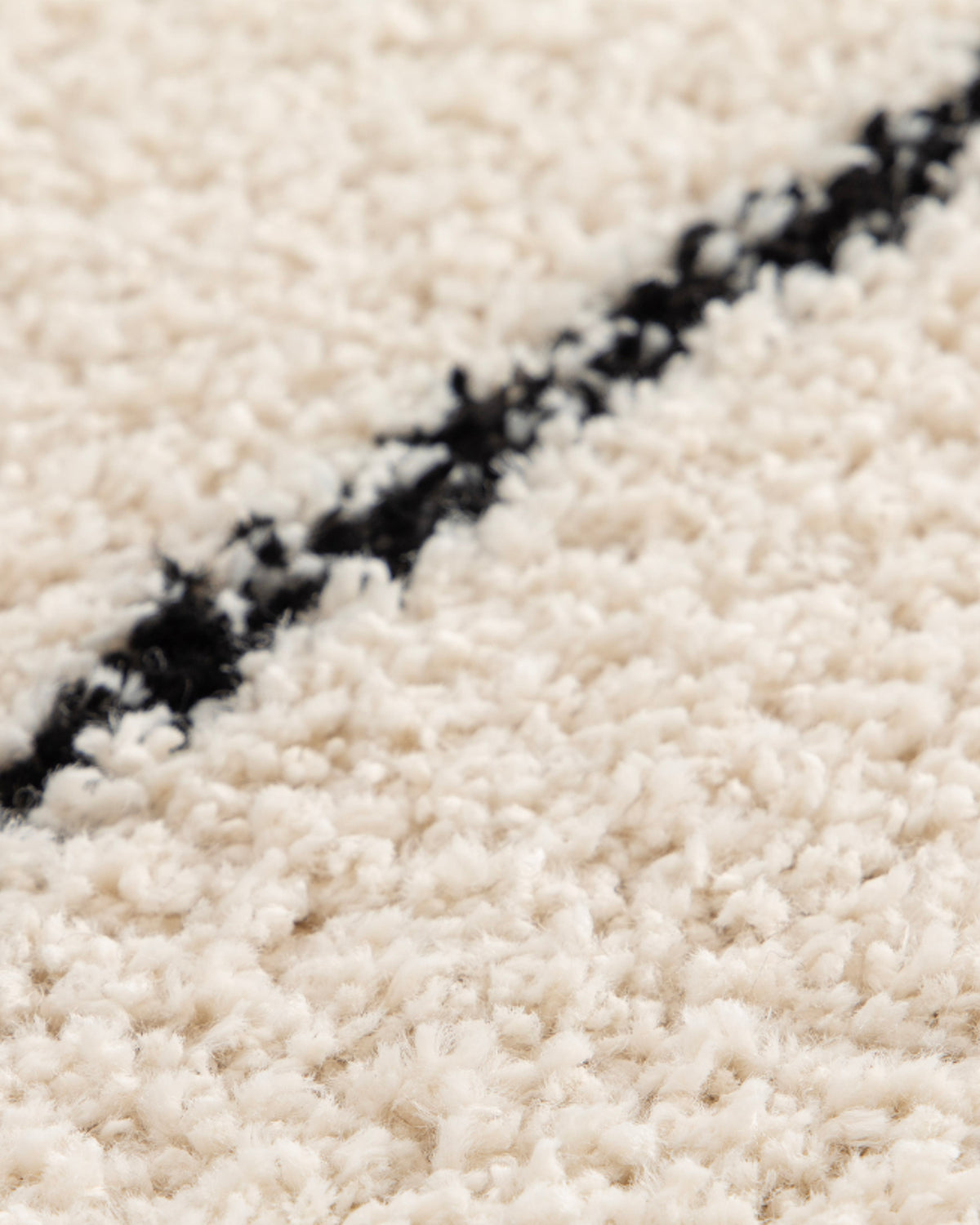 gros plan sur la ligne noire droite qui divise un tapis de salon Kento en velours écru
