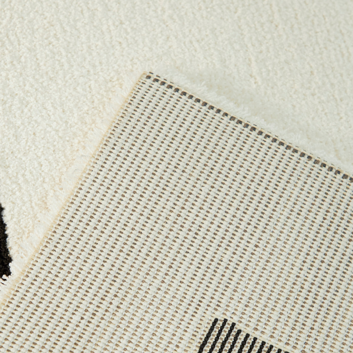 coin replié du tapis ARCA, hauteur du velours écru et envers tissé beige et noir