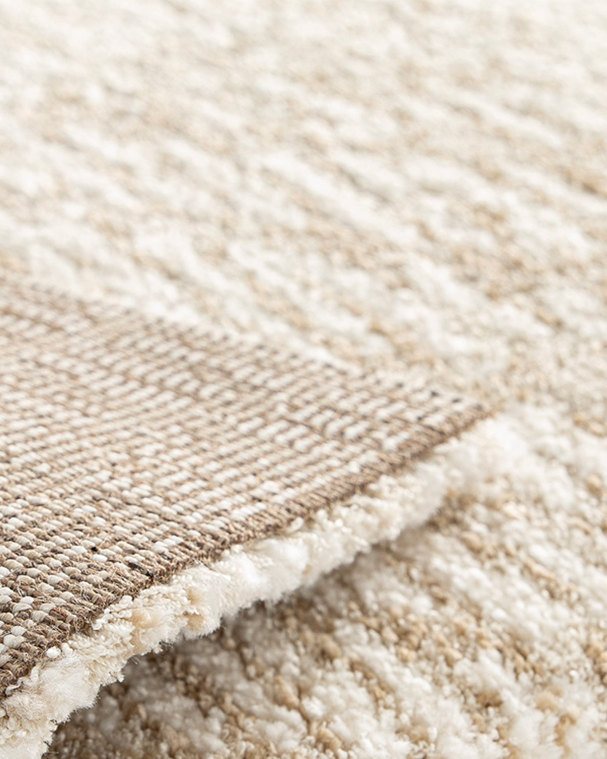 gros plan sur l'envers tissé beige et la lisière surjetée d'un tapis de salon Cortex écru