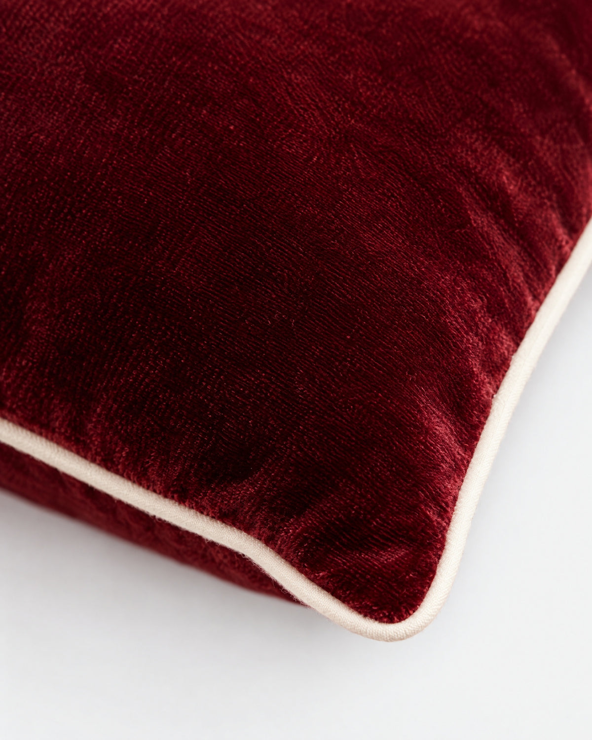 gros plan sur le passepoil écru et la texture du velours rouge bordeaux du coussin LODGE